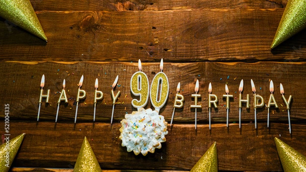 Obraz golden letters of the candle with the number happy birthday, the background of the pie with candles happy birthday on the background of brown stranded boards. Postcard Happy birthday 90