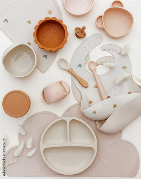 Obraz Top view silicone dishware plate and spoon. Serving baby, first feeding concept. Kids tableware and bib on light background. Flat lay, copy space, top view