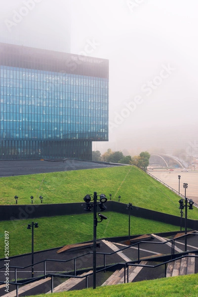 Fototapeta Katowice, Poland - 14 October 2021: Cultural Center in Katowice. View towards a modern skyscraper on a hazy day. Green roofs in the foreground.