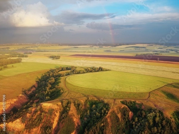 Obraz From a height, a view of high hills with fields of grass and groves of birches. Erosion of clay hills. Rainbow illuminated by the evening sun