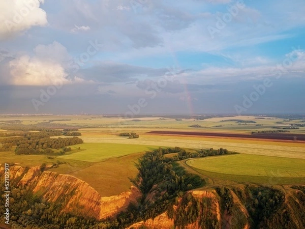 Obraz From a height, a view of high hills with fields of grass and groves of birches. Erosion of clay hills. Rainbow illuminated by the evening sun
