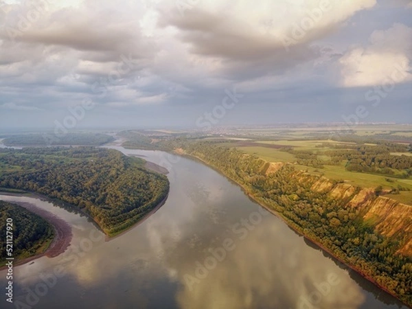 Obraz Riverbed under the mountain and groves of trees on the shore. Evening light of the sun. Clouds in the sky and reflection in the water. River Ob