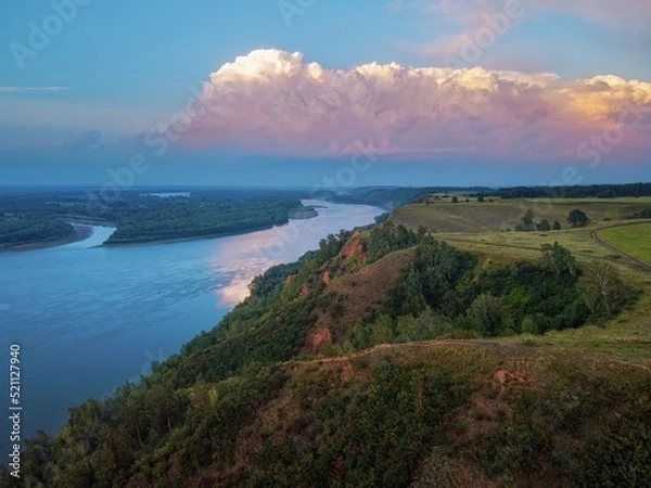 Obraz a high bank of clay with fields and trees, clouds in the sunset light, the sun and the riverbed of the Ob