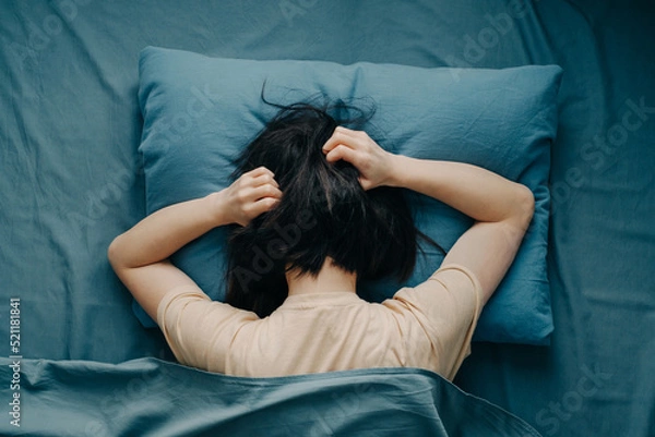 Obraz The young woman in bed hugged her head. Depression or mental health problems. Top view.