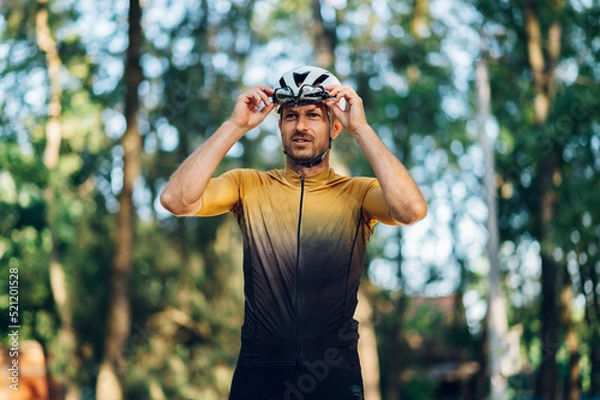Fototapeta Athletic man in sport clothes riding a bike in the nature and posing with glasses