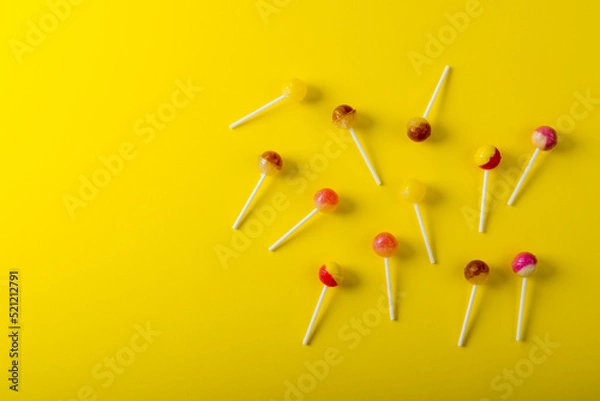 Fototapeta Overhead view of lollipops scattered by copy space against yellow background