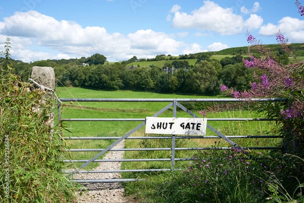 Fototapeta A hand painted shut gate sign attached to a metal gate at the entrance to a footpath running through green countryside in summer