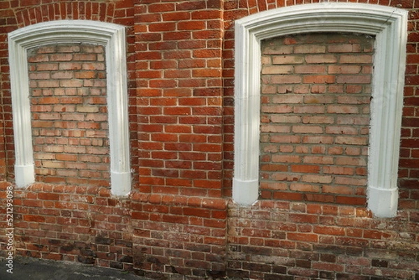 Fototapeta Aged brick wall with four arched bricked up windows with space for text.