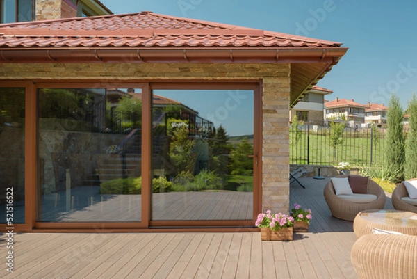 Obraz Exterior view of the terrace of a modern country house. Large glass windows reflecting the cozy courtyard. Wooden floor and wicker garden furniture