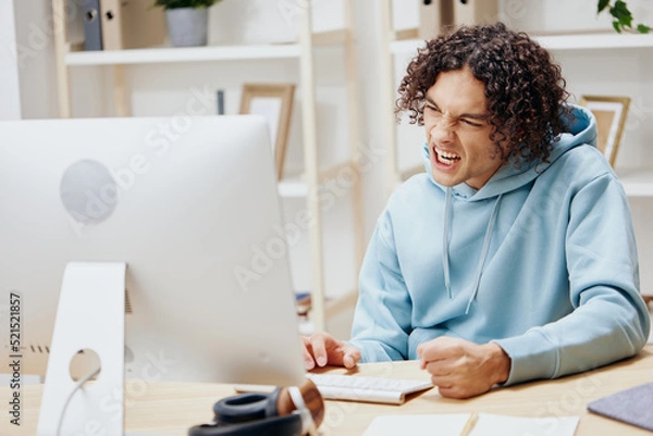 Fototapeta guy with curly hair in a blue jacket in front of a computer technologies