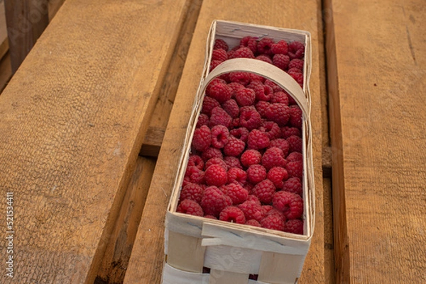 Fototapeta This is a basket with raspberries on a wooden background.