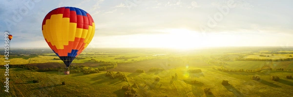 Obraz Colorful hot air balloons fly over the fields at sunset on a warm autumn evening. Panorama of a beautiful landscape in the sunlight from a bird's eye view.