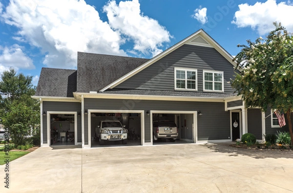 Fototapeta The side view of a large gray craftsman new construction house with a landscaped yard a three car garage and driveway