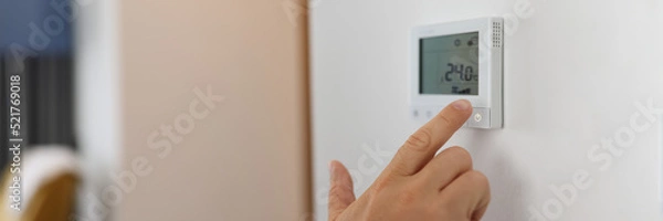 Fototapeta Hand sets a programmable thermostat for heating and cooling