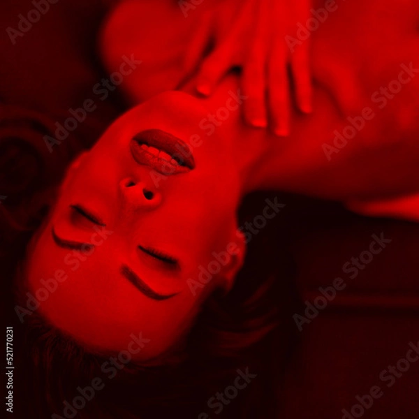 Fototapeta Passionate woman laying on sofa with closed eyes in red light