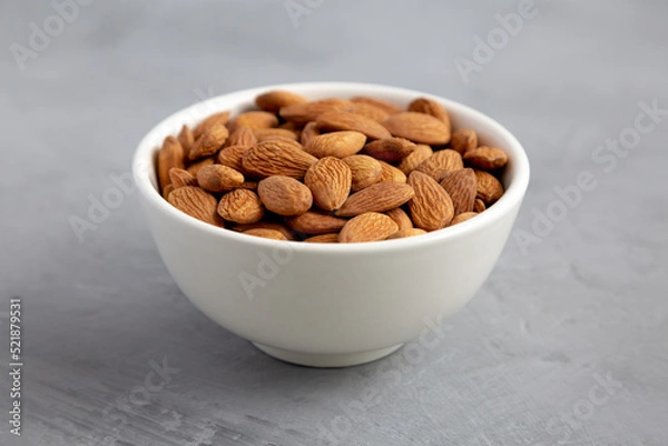 Fototapeta Raw brown almonds in a bowl on a gray background, low angle view. Close-up.