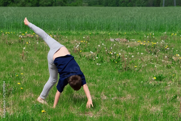 Obraz Boy makes an acrobatic wheel. On the grass. close up