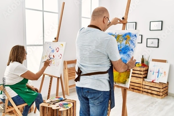 Fototapeta Middle age hispanic painter couple on back view painting at art studio.