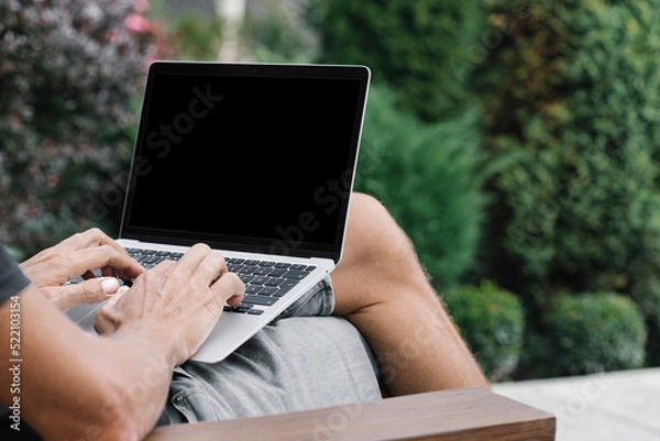 Fototapeta a man works in nature, sitting in a chair with a laptop