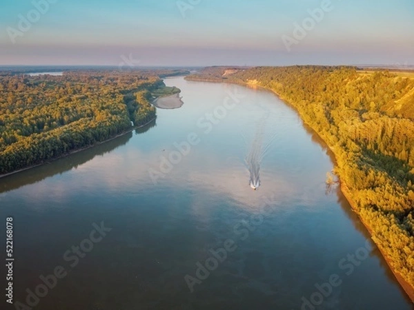 Obraz River valley with a steep bank with a forest of trees, sunlight and a boat on the water
