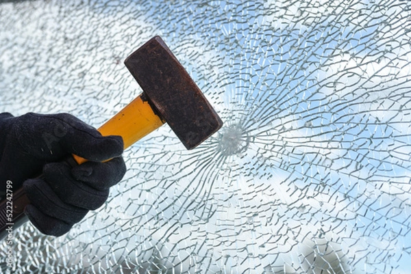 Fototapeta Man’s hand is hitting a window from safety glass with a heavy hammer, vandalism and burglary concept, copy space