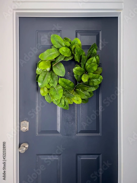 Fototapeta Front view of a navy blue door with a colorful green wreath on a bright, sunny day