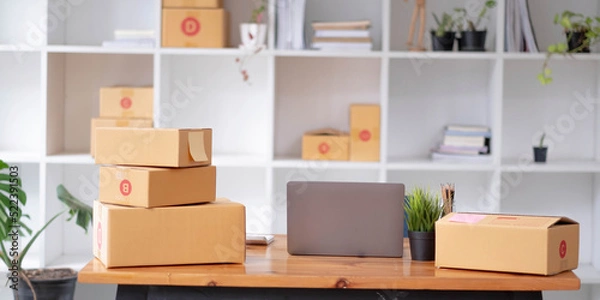 Fototapeta Parcel boxes on shelf and color shopping bags placing near laptop on table. SME business on shopping online at home office packaging on background is popular business.