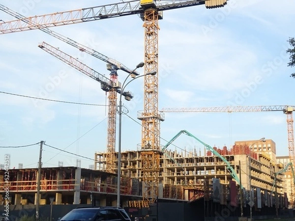 Obraz Full-color horizontal photo. A huge construction site. Several tower cranes and other large construction equipment. A grid of supports with fittings and floor coverings.