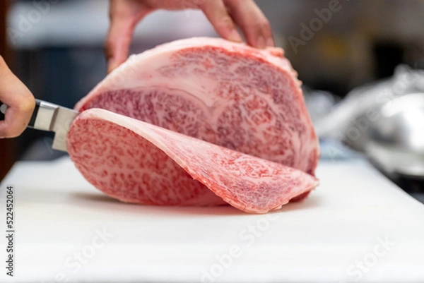 Obraz 和食レストランの厨房で板前が丁寧に切り分ける、見事な霜降りの最高級和牛サーロインブロック肉の調理シーン。テキストを入れるスペースあり