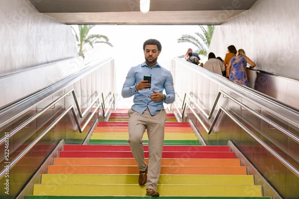 Fototapeta Latin american man with dreadlocks walks down colorful stairs with a mobile phone