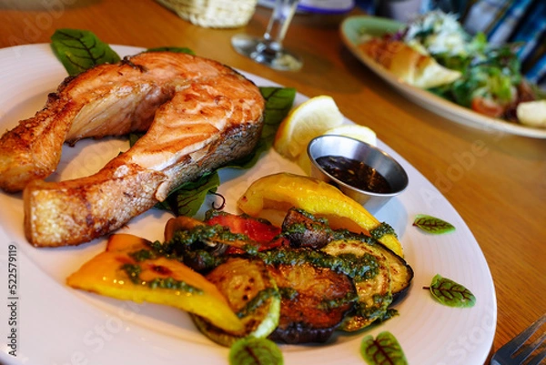 Fototapeta Grilled salmon with vegetables, lemon and pesto sauce. Serving the dish. Shallow depth of field