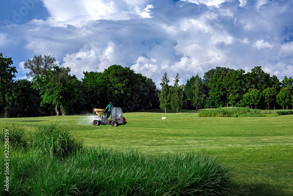 Fototapeta transport specialized equipment for fertilization and lawn care on a golf course, gardening supplying plants with nutrients on a hilly landscape on a sunny day with clouds on the sky.