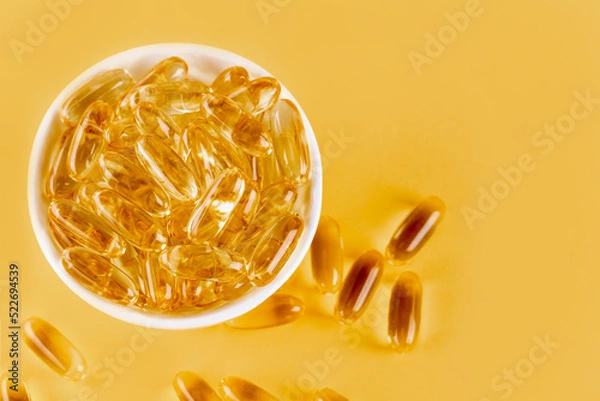 Fototapeta Omega 3 capsules lying on yellow background. Fish oil in pills. Health support and treatment. Biologically active additives. Selective focus.