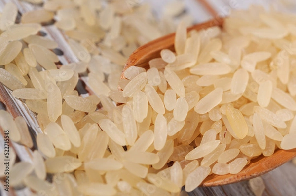 Obraz Rice groats scattered on a light wooden background closeup. Shallow depth of field