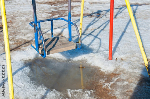 Fototapeta Multi-colored metal and wooden swing on the snow-covered playground