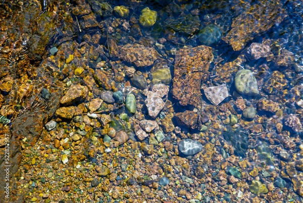 Fototapeta Small stones at the bottom of the river under a layer of clear water. Background from stones. Texture of water and stones.