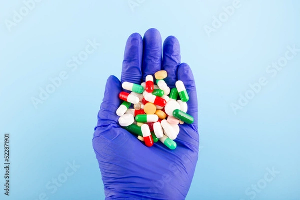 Obraz Hand in a blue medical glove with a handful of tablets and pills. Medicine concept.
