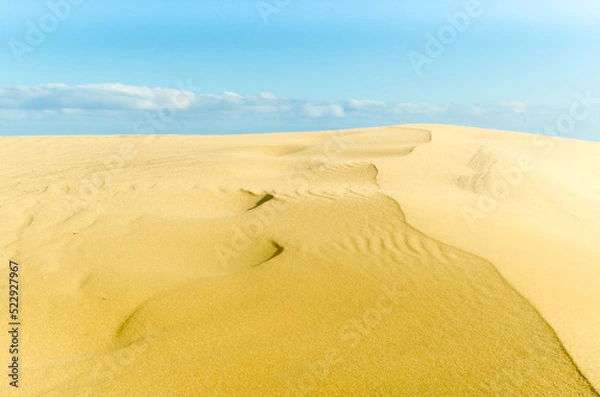 Fototapeta Sand dunes in a desert with blue sky and clouds in the background