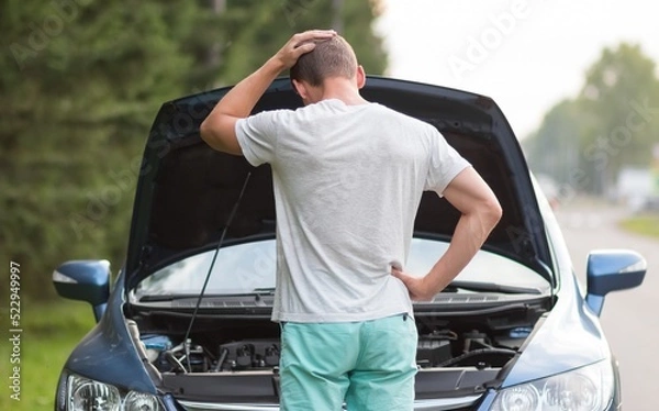 Fototapeta A man stands near the open hood of a car. The car needs repair