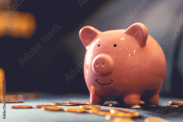 Obraz Um cofrinho sobre um sofá azul com moedas espalhadas. Conceitos de finanças do lar e economia.