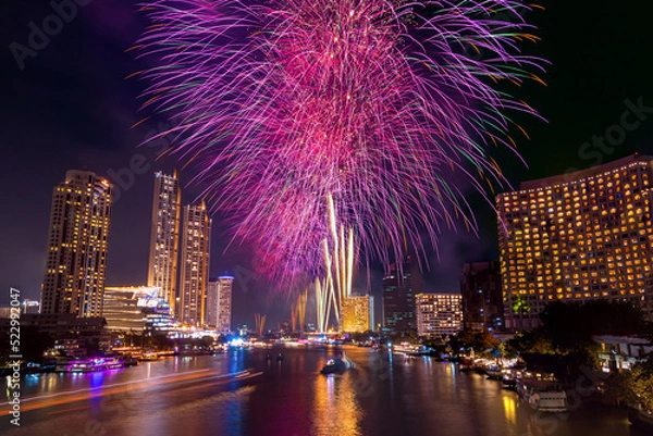 Fototapeta Colorful Firework at river with cityscape night light view of Bangkok skyline at twilight time..New Year celebration fireworks, Thailand.Fireworks light up to sky at Christmas and New Year festival