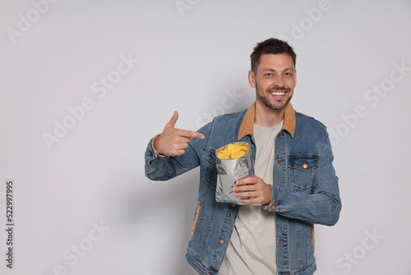 Obraz Handsome man pointing on potato chips against light grey background. Space for text