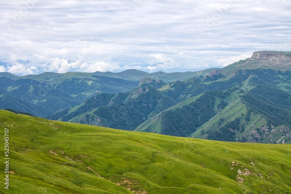 Fototapeta Beautiful landscape - panoramic view of green mountains and hills blurred in morning haze from bermamyt plateau in karachay-cherkessia Russia and dramatic clouds and copy space