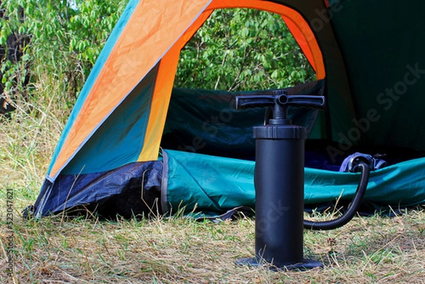 Fototapeta air mattress pump with a tent on a background in a pine forest in the summer, a man pumps up a mattress, a pump between his legs, the pump inflates the mattress, the pump inflates the air mattress in 