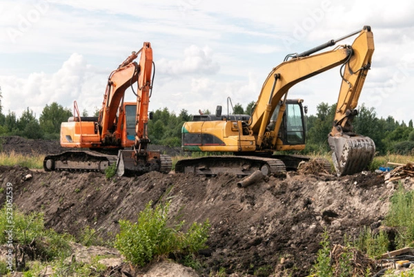 Fototapeta Crawler excavators dig the earth with a bucket. Drainage of swamps. Clearing the construction site. Peat mining. Road construction works.
