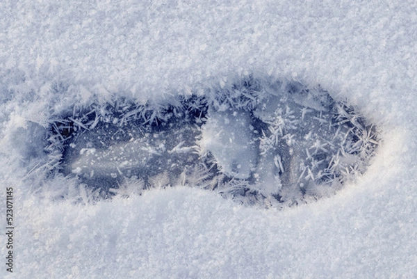 Fototapeta A human footprint in the snow and large snowflakes