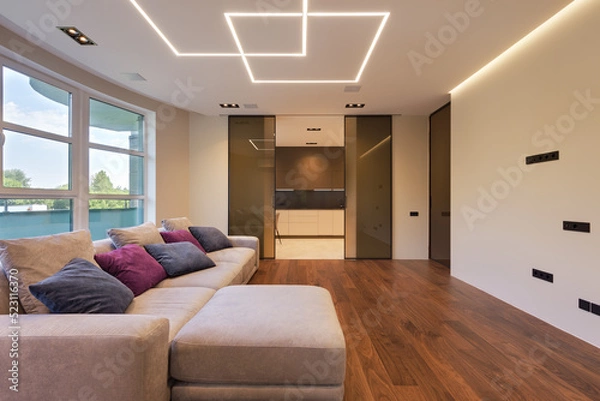 Obraz living room in a modern city apartment with designer lighting and sliding doors, living room in a modern apartment with a large gray sofa
