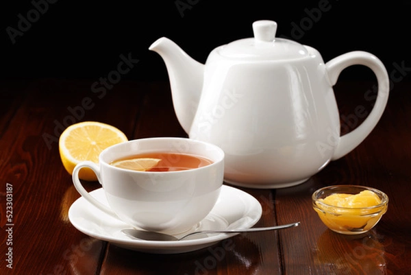 Obraz Tea with lemon and honey in a porcelain cup against a black background. Ceramic tea utensils. Side view. Selective focus.