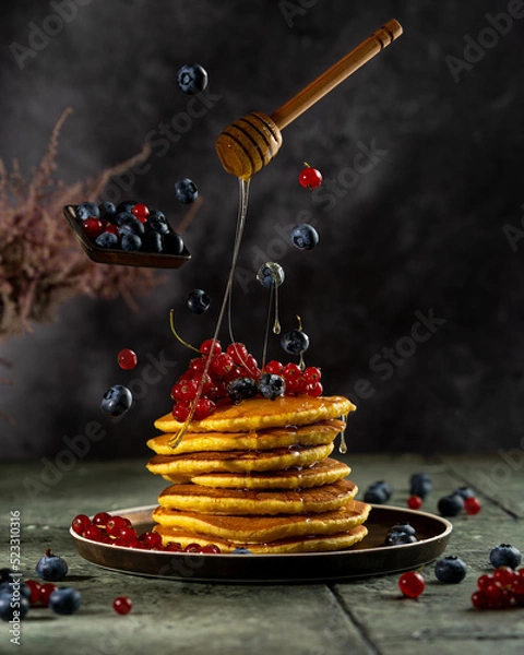 Fototapeta Homemade pancakes stack with fresh berries and honey on dark background, beautiful conceptual levitation studio picture, flying food art. Sweet pastry, copy space.
