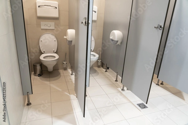 Fototapeta Pair of classic toilet cubicles with an open door in a public restroom